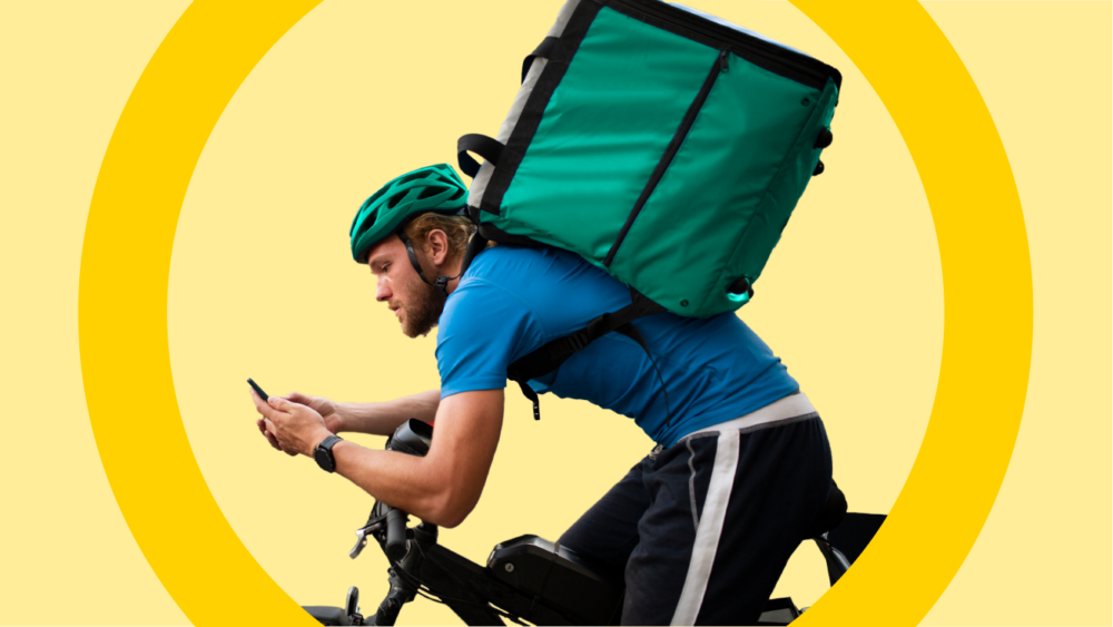 A bicycle delivery person with a large food delivery bag looking at their phone