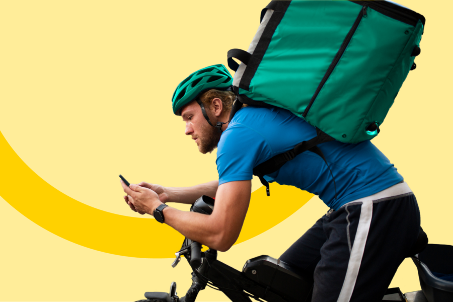 Person sy’n dosbarthu nwyddau ar feic gyda bag dosbarthu bwyd mawr yn edrych ar ei ffôn.