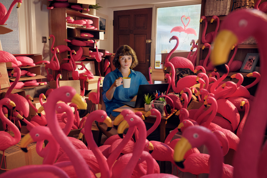 Woman on a laptop holding a cup of coffee surrounded by flamingos